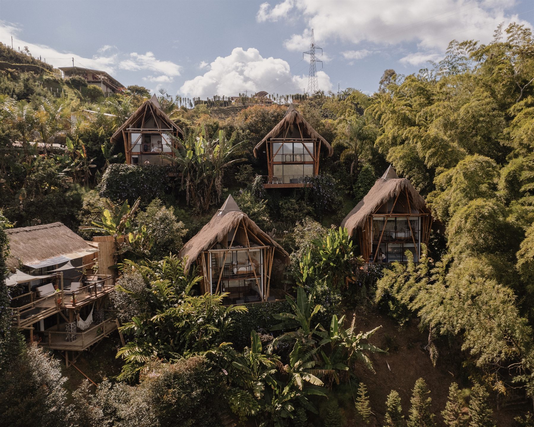 Vista aérea con drone de varias cabañas de bambú de IBUKU con techo de paja entre la vegetación tropical de Guatapé